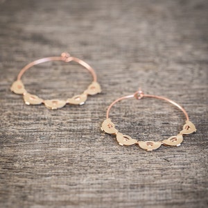 May include: A pair of gold hoop earrings with a decorative design of half-circles around the hoop.