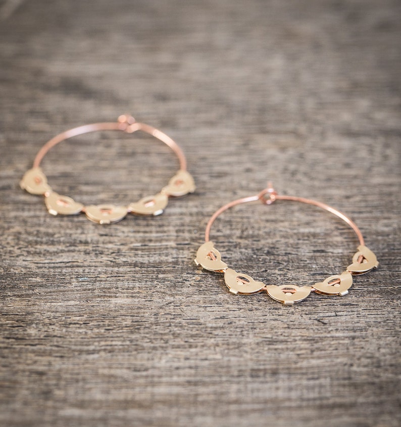 May include: A pair of gold hoop earrings with a decorative design of half-circles around the hoop.