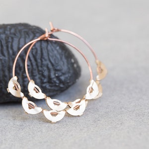May include: Rose gold hoop earrings with a delicate design of overlapping half-circles.
