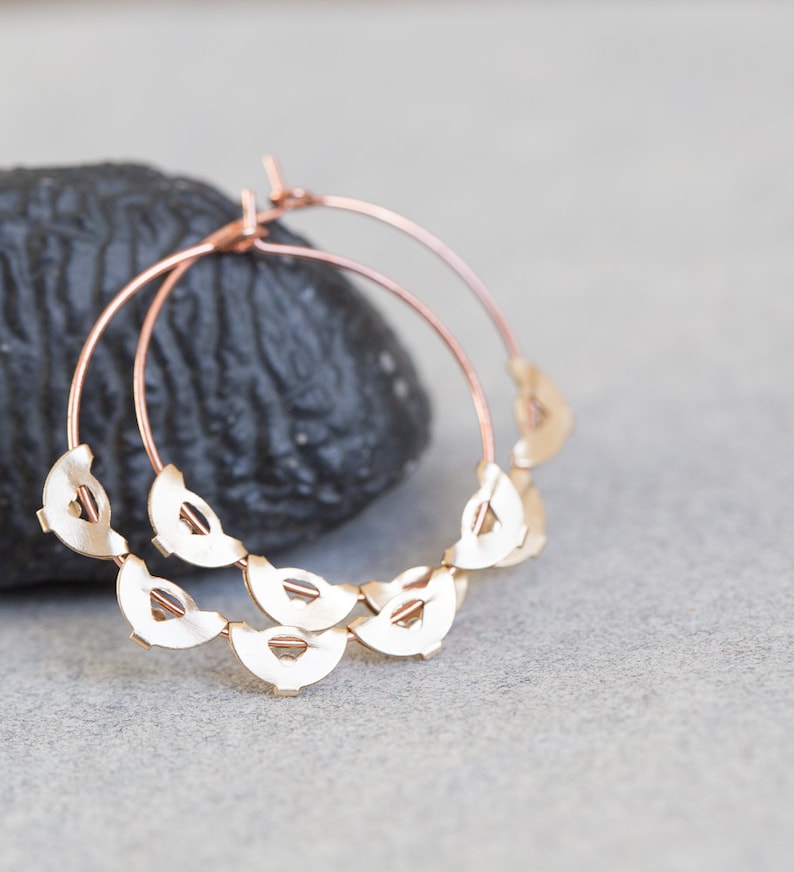 May include: Rose gold hoop earrings with a delicate design of overlapping half-circles.