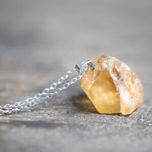 May include: A silver chain necklace with a raw, yellow citrine pendant. The pendant is a natural, rough-cut stone with a translucent, golden colour.