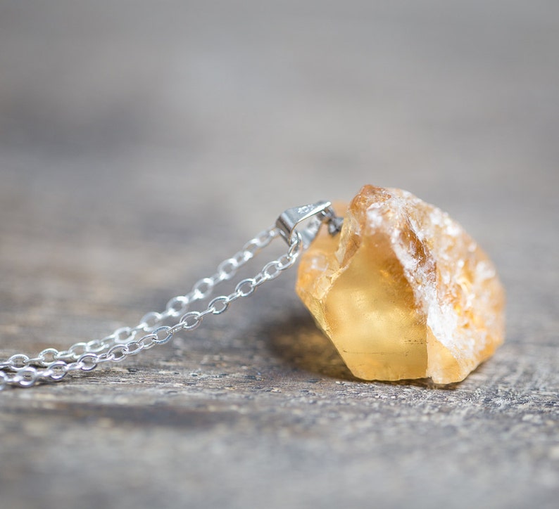 May include: A silver chain necklace with a raw, yellow citrine pendant. The pendant is a natural, rough-cut stone with a translucent, golden colour.