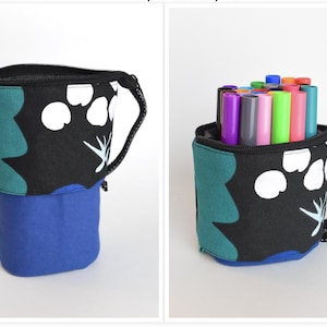 May include: A cylindrical fabric pencil case with a black top featuring white and teal abstract shapes, and a solid blue bottom. The case has a black zipper closure and a side handle. One view shows the case empty, the other filled with markers.