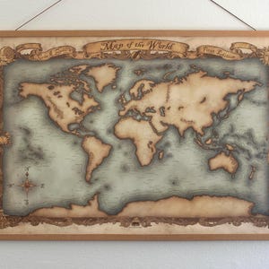 May include: A vintage-style world map print, framed with a wooden border and suspended by a string. The map features a detailed depiction of continents and oceans in muted tones, with decorative scrollwork and the text "Map of the World".