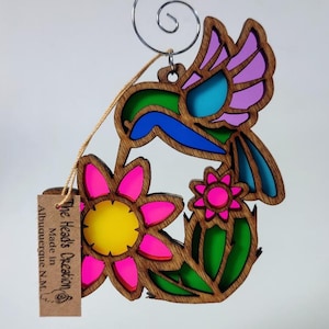 May include: Wooden hummingbird ornament with colorful stained glass accents, featuring a pink flower and green leaves. The ornament is made by The Head's Creation in Albuquerque, NM.