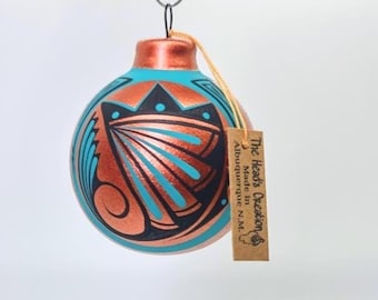 Puede incluir: Adorno navideño redondo con acabado color cobre y diseños geométricos turquesa y negro. La etiqueta dice "The Head's Creation, Made in Albuquerque N.M."