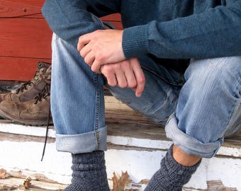 May include: A pair of dark charcoal gray knit socks with a ribbed texture at the ankles. The socks are crafted from a heathered yarn material, featuring a mid-calf length and a thick, cozy construction suitable for warmth and comfort during colder weather.