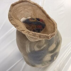 May include: A beige nylon stocking filled with a dark, multi-colored object. The stocking is open at the top, revealing the contents. The object appears to be a bundle of hair or fibers, with hints of red, black, and brown.