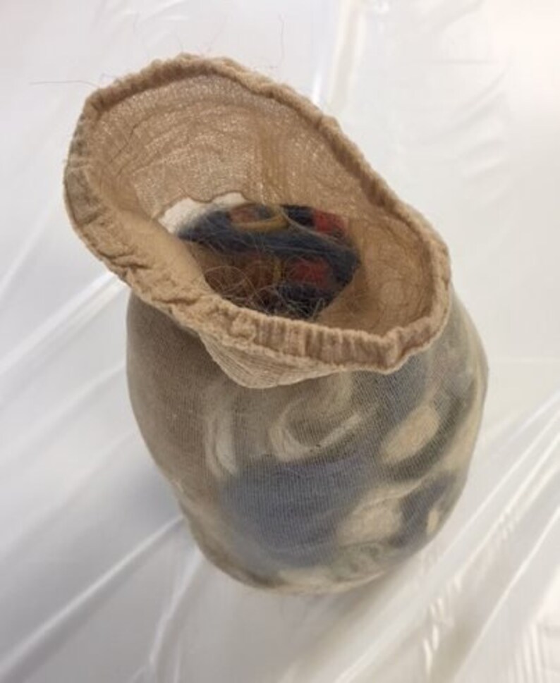 May include: A beige nylon stocking filled with a dark, multi-colored object. The stocking is open at the top, revealing the contents. The object appears to be a bundle of hair or fibers, with hints of red, black, and brown.