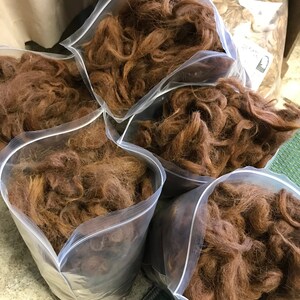 May include: Several clear plastic bags filled with brown fiber. The bags are sealed with a zipper closure. The fiber appears to be a natural material, possibly wool or alpaca, and is a warm, reddish-brown color.