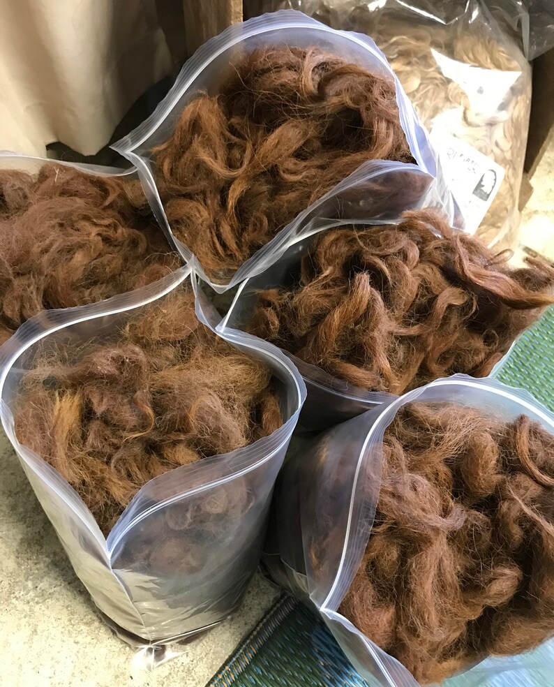 May include: Several clear plastic bags filled with brown fiber. The bags are sealed with a zipper closure. The fiber appears to be a natural material, possibly wool or alpaca, and is a warm, reddish-brown color.