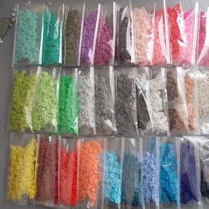 May include: A selection of colourful sequins in small, clear plastic bags. The sequins are in a variety of colours, including yellow, red, orange, blue, and purple. The sequins are small and round, and appear to be made of plastic.