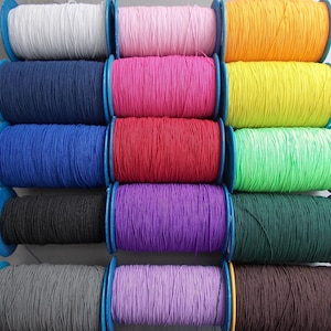 May include: A selection of elastic cord spools in a variety of colours: white, pink, orange, navy, hot pink, yellow, blue, red, green, black, purple, and brown. The spools have blue plastic sides.