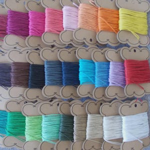 May include: A selection of colourful twine spools arranged in rows. The spools are made of cardboard and hold various shades of twine, including pink, purple, blue, green, orange, and yellow. The twine is tightly wound on the spools.