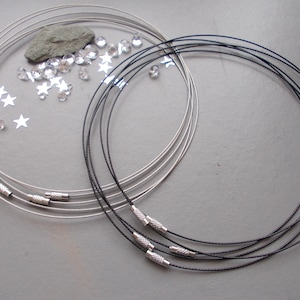 May include: Two sets of necklace wires, one silver and one black, with silver clasps. The silver set is next to a collection of clear crystals, a grey stone, and star-shaped sequins. The black set is on the right side of the image.
