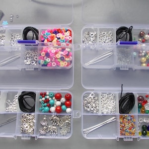 May include: Four clear plastic organiser boxes filled with jewellery-making supplies. The boxes contain various beads in multiple colours, silver-toned clasps, black cords, and head pins. Some boxes have a variety of colourful beads, including red, turquoise, and white.
