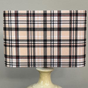 Puede incluir: Una lámpara de mesa de cerámica beige con una pantalla rectangular con un patrón de cuadros negros, blancos y rojos.