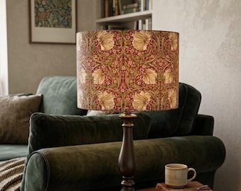 May include: A table lamp with a dark bronze-toned metal base and a cylindrical lampshade featuring a repeating botanical pattern in shades of deep red, muted green, and cream, depicting stylized tulip-like flowers and intricate leafy vines.