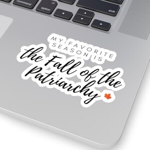 Può includere: Un adesivo bianco con testo nero in corsivo che recita "the Fall of the Patriarchy". Sopra il testo c'è "MY FAVORITE SEASON IS" in un carattere più piccolo e squadrato. Una piccola foglia d'acero arancione si trova nell'angolo in basso a destra.