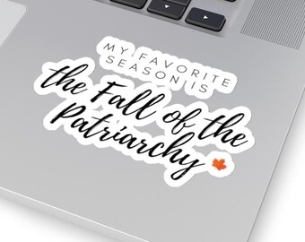 Op de afbeelding: Een witte sticker met zwarte cursieve tekst die luidt "the Fall of the Patriarchy". Boven de tekst staat "MY FAVORITE SEASON IS" in een kleiner, blokkerig lettertype. Een klein oranje esdoornblad staat in de rechter benedenhoek.