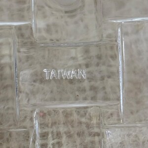 Może przedstawiać: Zbliżenie przezroczystego szklanego przedmiotu z wzorem kratki. Słowo "TAIWAN" jest wytrawione w szkle. Tło ma miękki, neutralny odcień.