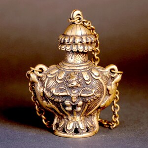 May include: A gold-colored metal bottle with intricate carvings and a chain. The bottle has a domed lid and a small figure of a mythical creature on the front.