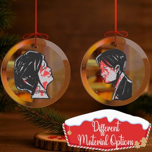 Puede incluir: Dos adornos redondos y transparentes con cuerdas rojas para colgar. Cada adorno presenta una ilustración de perfil en negro y rojo. Los adornos se exhiben sobre una superficie de madera con un letrero que dice "Different Material Options".
