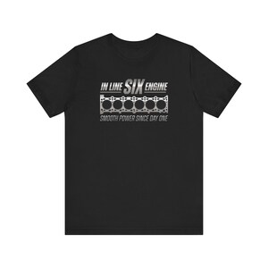 May include: Black t-shirt with the text "IN LINE SIX ENGINE" in silver and a graphic of an engine block. The phrase "SMOOTH POWER SINCE DAY ONE" is printed below the engine graphic.