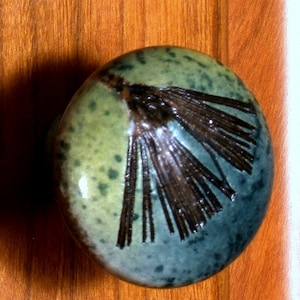 May include: A green and blue ceramic door knob with a brown design. The knob has a speckled glaze and a unique design.