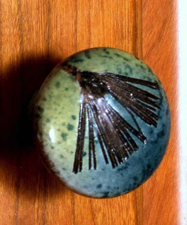 May include: A green and blue ceramic door knob with a brown design. The knob has a speckled glaze and a unique design.