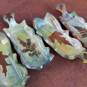 May include: Four ceramic serving dishes with scalloped edges and leaf designs. The dishes are glazed in shades of green, brown, and yellow.