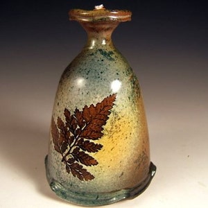 May include: A ceramic vase with a light blue, green, and yellow glaze. The vase features a fern design in brown on the front.