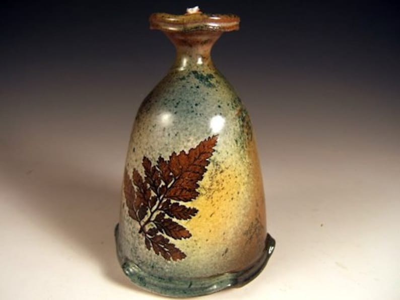 May include: A ceramic vase with a light blue, green, and yellow glaze. The vase features a fern design in brown on the front.