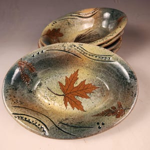 May include: Set of four oval ceramic bowls with a rustic, earthy glaze. Each bowl features a different leaf design in shades of brown and green.