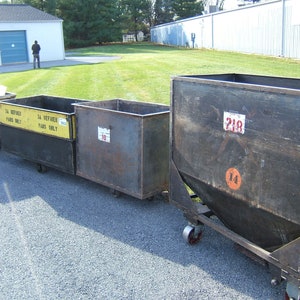 May include: Four metal industrial bins on wheels. The bins are gray and have numbers painted on them. The bins are lined up in a row. The bin on the far right has the number 218 painted on it. The bin in the middle has the number 18 painted on it. The bin on the left has the number 317 painted on it. The bin in the middle has the text "3A REFINER PARTS ONLY" painted on it.