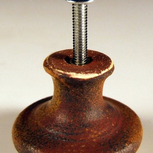 May include: A brown ceramic knob with a silver screw. The knob has a textured surface and a rounded base.