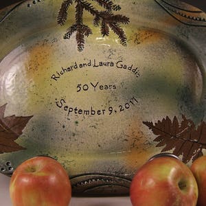 May include: A ceramic serving platter with a rustic, hand-painted design. The platter features a leafy pattern and the inscription "Richard and Laura Gaddis 50 Years September 9, 2011".