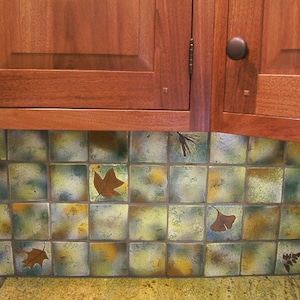 May include: A kitchen backsplash with a tile pattern of green, brown, and yellow squares with leaf designs.