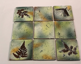 May include: Nine square ceramic tiles with a green and yellow background. Each tile features a brown pressed leaf design. The leaves include ferns and pine needles.
