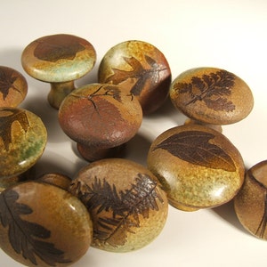 May include: A collection of nine ceramic knobs with various leaf designs. The knobs are brown, green, and beige with a glossy finish.