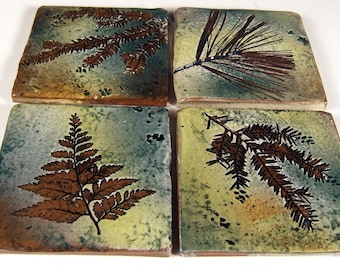 May include: Set of four square ceramic tiles with a nature theme. Each tile features a different type of leaf in brown and green tones on a light green, blue, and brown background.