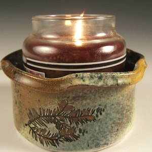 May include: A brown ceramic candle holder with a leafy design and a lit candle inside.