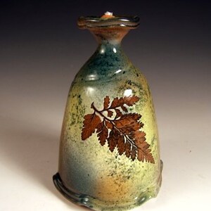 May include: A ceramic oil lamp with a green and brown glaze. The lamp features a fern design in brown on the front.