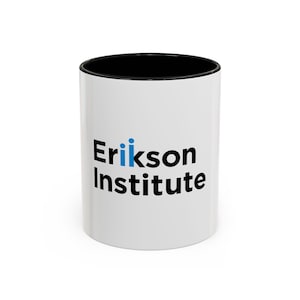Könnte beinhalten: Weiße Keramiktasse mit schwarzem Rand und Henkel. Die Tasse hat eine schwarze Grafik mit der Aufschrift "Erikson Institute" und eine blaue Grafik mit drei Personen, die neben dem Wort "Erikson" stehen.