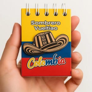 Peut inclure: Un petit carnet à spirales avec une couverture jaune, bleue et rouge portant le texte Sombrero Vueltiao et Colombia. Le centre de la couverture présente une illustration graphique d'un chapeau traditionnel à motifs noirs et beiges.