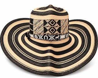 May include: A wide-brimmed straw hat featuring alternating black and natural tan concentric rings. The crown displays a geometric woven pattern in black and tan. A decorative band encircles the base, featuring white symbols including a horseshoe and a horse.