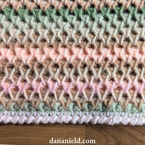 May include: Close-up of a hand-crocheted textile with a textured, woven appearance. The color palette includes soft pinks, greens, and browns, creating a subtle, blended effect. The bottom edge features a white border. The website address dananield.com is visible.