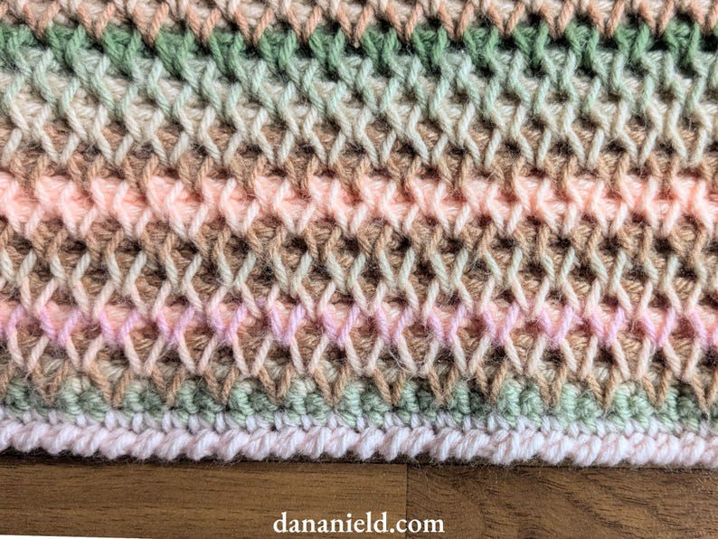 May include: Close-up of a hand-crocheted textile with a textured, woven appearance. The color palette includes soft pinks, greens, and browns, creating a subtle, blended effect. The bottom edge features a white border. The website address dananield.com is visible.