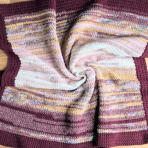 Puede incluir: Una manta de ganchillo hecha a mano en tonos burdeos, rosa y dorado. La manta presenta un patrón de puntada texturizada y un borde burdeos liso. Esta manta suave y cálida es perfecta para acurrucarse. Mide aproximadamente 150 cm x 150 cm.