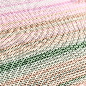 May include: A hand-knitted blanket with a gradient of colors, including pink, green, and tan. The blanket has a textured appearance and is made of soft yarn. The website address dananield.com is visible in the image.